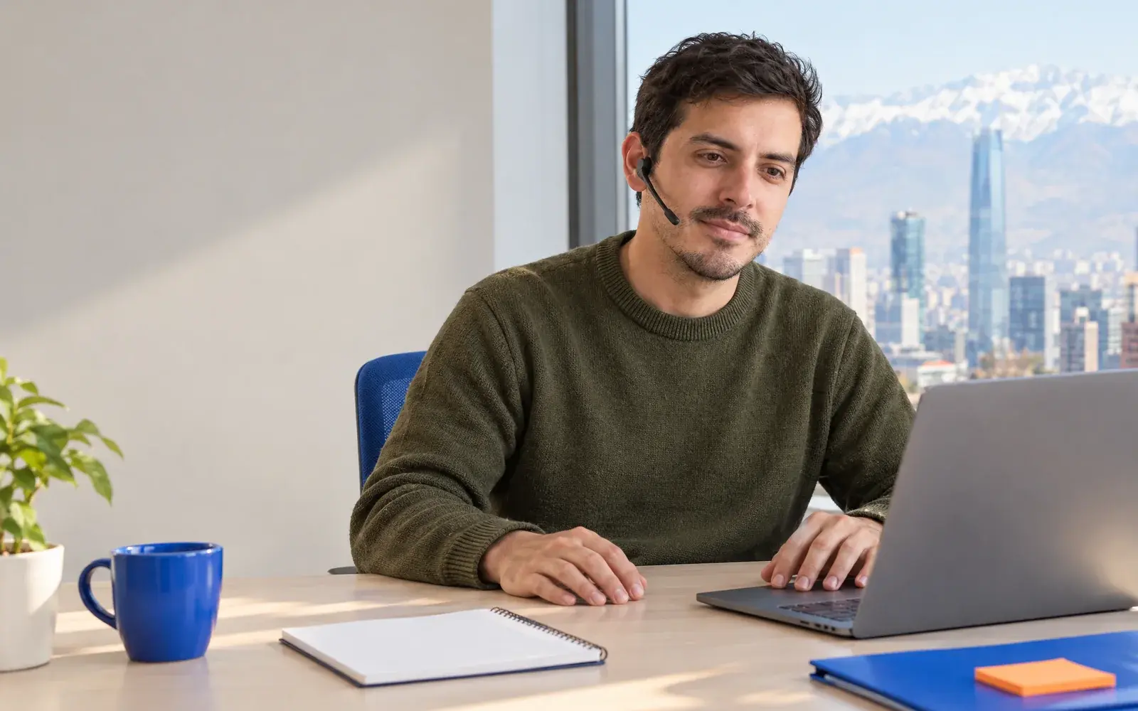 Una persona con audífono atiende una llamada junto a una laptop.